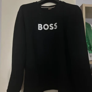 Svart sweatshirt från BOSS - Jätte fin Hugo boss tröja , köpt för cirka 2 månader sedan använt fåtal gånger. Inga hål eller slitage på den , Storlek L men passar över M
