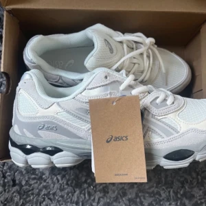 Vita och grå Asics sneakers - Snygga Asics sneakers i vitt och ljusgrått med mesh och syntetpaneler. Skorna har Ortholite komfortinnersula och coola detaljer på sulan. Perfekta för dig som gillar sportig och clean stil. Klassisk snörning och rund tå.