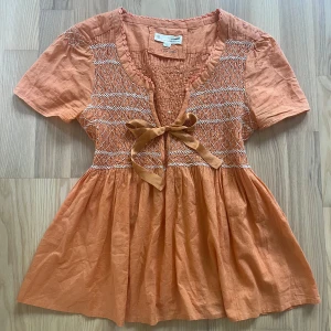 Persikofärgad blus från Odd Molly - Supersöt persikofärgad blus från Odd Molly med korta ärmar, broderade detaljer och knytband framtill. 