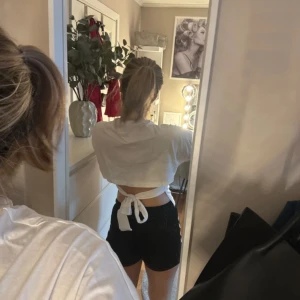 Vit croppad topp med knyt från Nelly - Säljer en vit croppad topp från Nelly i bomull. Toppen har korta ärmar, hög hals och snygg knytning i ryggen som ger en cool och trendig look. Perfekt för dig som gillar stilrena plagg med en twist.