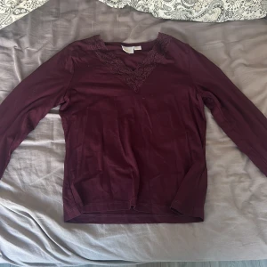 Vinröd långärmad topp med spets Gina Tricot - Säljer en vinröd långärmad topp från Gina Tricot med snygg v-ringning och dekorativ spets runt halsen. Toppen är i mjukt material och har en figurnära passform som passar perfekt till jeans eller kjol.