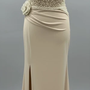 Champagnefärgad långklänning med pärlor - Elegant långklänning i champagnefärg med pärlbroderad överdel och en stor dekorativ blomma i midjan. Kjolen har en snygg slits framtill och draperade detaljer som ger en lyxig känsla. Perfekt för dig som vill sticka ut på bal eller fest. Storlek34/36