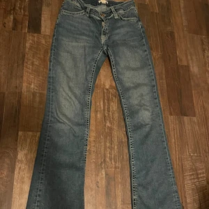 Blå bootcut jeans med kontrastsömmar - Snygga blå bootcut jeans med ljusa kontrastsömmar och detaljerade bakfickor med knappstängning. Jeansen har klassisk femficksdesign och är tillverkade i slitstarkt denimtyg. Perfekt för dig som gillar retrovibbar och markerade fickor.