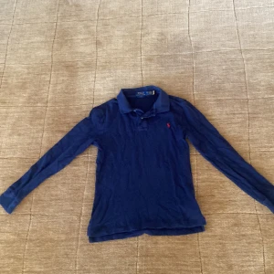 Blå långärmad piké Polo Ralph Lauren - Snygg blå långärmad piké från Polo Ralph Lauren i slim fit-modell. Klassisk krage och röd Polo logga broderad på bröstet. Inga fläckar