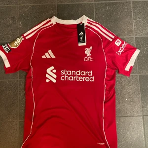 Liverpool FC fotbollströja med ISAK #9  - Säljer en Liverpool FC hemmatröja i bra skick med trycket Isak #9 på ryggen. Klassisk röd design från Liverpool FCs hemmaställ – perfekt för dig som vill visa stöd för klubben eller bara ha en snygg fotbollströja. 