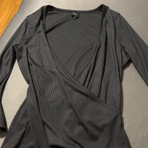 Svart Topp med v-ringning - Svart ribbad tröja från River Island med djup v-ringning och långa ärmar. Tröjan har en smickrande passform och är tillverkad i ett stretchigt material som sitter snyggt på kroppen. Perfekt för dig som gillar stilrena och trendiga plagg.