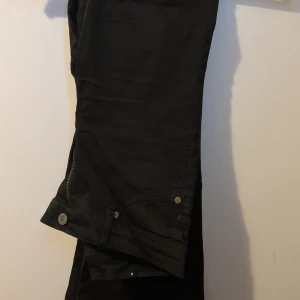 Svarta jeans med dragkedja vid benslut - Svarta jeans med snygga detaljer som dragkedja och knapp vid benslutet. Klassisk femficksmodell med raka ben och stilren look. Perfekta för dig som gillar en enkel men cool stil.