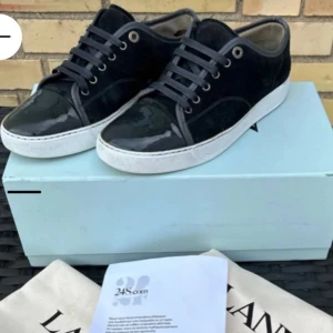 Svarta sneakers från Lanvin i mocka - Snygga svarta sneakers från Lanvin med ovandel i mocka och lackad tå. Skorna har vita sulor, svarta skosnören och diskreta silverfärgade metalldetaljer vid snörningen. Det är lite söndrigt i hälen. Det är stora i storlek och passar mer som 42 även om det är i storlek 41. Anledning till det billiga priset är för att det har lite defekter på hälen