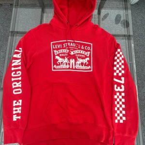 Vintage Levi’s röd hoodie L – unisex streetwear i toppskick - Snygg röd hoodie från Levi’s i storlek L. ✔ Ikoniskt Levi Strauss & Co. logotyptryck framtill ✔ Vänster ärm med “The Original” ✔ Höger ärm med schackrutor + 1873 ✔ Klassisk känguruficka och huva med dragsnören ✔ Mjuk insida, mycket bra skick – nästan som ny ✔ Passar både dam & herr – perfekt unisex streetwear & vintage vibe  Perfekt för dig som gillar retro Levi’s, streetwear och hoodies av hög kvalitet.  Material: Bomull & polyester-blandning (mjukt och slitstarkt).