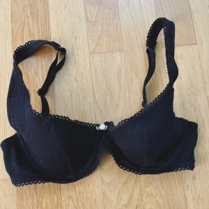 Svart bh - Svart bh med ribbad struktur och söt spetskant längs kuporna. Dekorerad med en liten ljusrosa ros i mitten framtill. Vet tyvärr inte strl men skulle gissa på 75 A/B💕