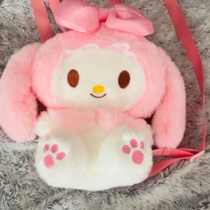Söt rosa my melody ryggsäck med rosett - Supergullig ryggsäck i form av en med stora öron, broderat ansikte och tassar. Aldrig använt, väskan är fluffig i rosa och vitt, har justerbara axelband och en stor rosa rosett upptill. Stängs med dragkedja och är perfekt för dig som älskar kawaii-stil.