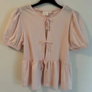 Ljusrosa blus med knyt från Gina Tricot - Supersöt ljusrosa blus från Gina Tricot med puffiga korta ärmar och tre knyt framtill. 