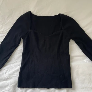 Svart långärmad topp med v-ringning - En svart långärmad topp med v-ringad hals och figurnära passform. Toppen är enkel och stilren, perfekt att matcha med jeans eller kjol. Materialet är mjukt och stretchigt, vilket gör den bekväm att bära hela dagen.