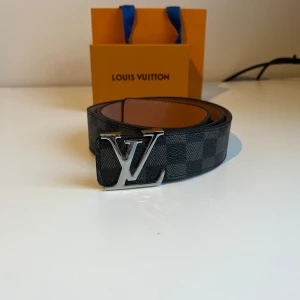 Svart bälte med silvrigt spänne - Snyggt bälte i klassiskt Damier-mönster i svart och grått. Bältet har ett spänne i silverfärgad metall och är gjort i exklusivt skinn med brunt foder. Perfekt accessoar för att lyfta din outfit. Med följer kvitto, box och påse. Priset kan sänkas vid snabb affär ✅