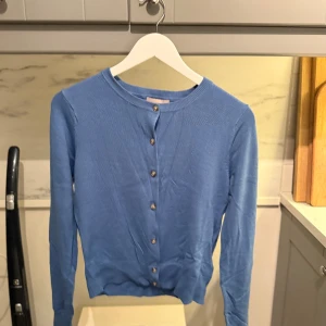 Blå kofta med knappar från H&M - Snygg blå kofta med knäppning framtill. Långärmad modell i mjukt material från H&M