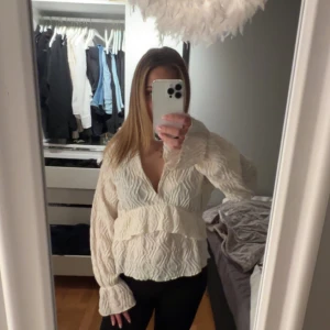Krämvit blus med volang - Säljer en krämvit omlottblus från Gina Tricot med v-ringning och volangdetaljer framtill. Blusen har långärmade ärmar. Använd få gånger.