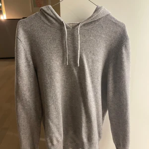 Grå hoodie i kashmir från Sayless - Mjuk och lyxig grå hoodie från Sayless i kashmir. Klassisk modell med huva och snörning, ribbade muddar och lång ärm. Perfekt för dig som vill ha en stilren och bekväm tröja med premiumkänsla.