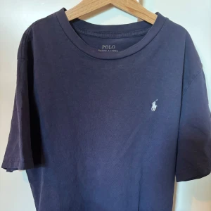 Mörkblå t-shirt från Polo Ralph Lauren - Klassisk mörkblå t-shirt från Polo Ralph Lauren med broderad logga på bröstet. T-shirten är i mjuk bomull, har rund halsringning och korta ärmar. Perfekt basic-plagg med stilren design och skön passform.