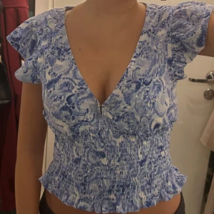 Blåvit blommig blus med volang - Supersöt blommig blus i blått och vitt med v-ringning och korta volangärmar. Använd endast en gång! 