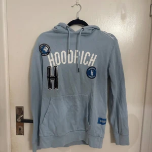 Ljusblå hoodie från Hoodrich - Säljer en ljusblå hoodie från Hoodrich i storlek S. Tröjan har vita och svarta tryck och patches framtill, snörning i huvan och en stor magficka. Perfekt för dig som gillar streetwear och vill ha en chill look. PRIS KAN DISKUTERAS !!