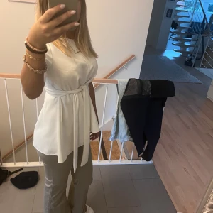 Vit omlottopp med knytband - Säljer en vit omlottopp med knytband i midjan och korta ärmar. Perfekt att styla med jeans eller kostymbyxor💗