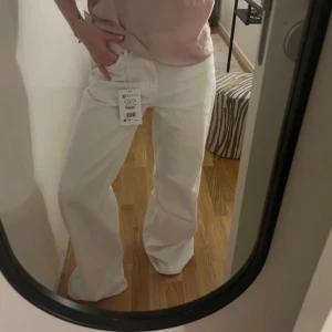 Vita baggy jeans från Pull&Bear - Säljer ett par vita baggy jeans från Pull&Bear i storlek 32. De har en avslappnad passform, raka ben och klassiska femficksdetaljer. Jeansen är tillverkade i bomull och har bälteshällor samt dragkedja och knapp framtill.