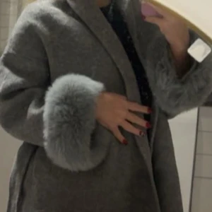 Kappa med pälsärmar - En jättefin trendig kappa med päls längst ärmarna. Det är äkta rävpäls och alpacka tyg. Den är varm och i bra skick. Använt en gång. Ska beställa annan färg. 
