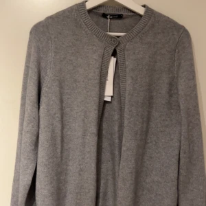 Grå kofta från Gina Tricot - En stilren gråmelerad kofta från Gina Tricot i storlek M. Koftan är stickad i mjuk bomullsblandning, har rund halsringning och stängs med en knapp upptill. Perfekt att slänga över en t-shirt eller topp för en chill look. Aldrig använd💞