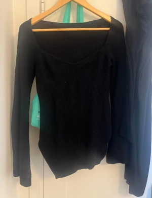 Svart ribbad stickad tröja - Svart stickad tröja med ribbad struktur och långärmad design. Tröjan har en snygg, bred och något fyrkantig halsringning som ger en modern vibe. Passformen är normal och materialet känns mjukt och skönt mot huden. Perfekt för att lyfta din outfit med en enkel men stilren look.