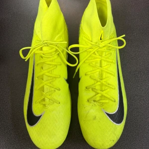 Nike Air Zoom fotbollsskor neongula - Säljer ett par Nike Air Zoom fotbollsskor i en riktigt fet neongul färg med svarta och silvriga detaljer. Skorna har snörning, högre strumpliknande skaft och metall-dobbar för gräsplan. Ovandelen är i syntetmaterial med NikeSkin för extra känsla på bollen.