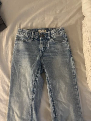 Ljusblå jeans från Lindex - Snygga ljusblå jeans från Lindex med klassisk femficksdesign och raka ben. Jeansen har normal midja och är tillverkade i mjukt denimtyg med lite stretch för extra komfort. Perfekta för en avslappnad och trendig look.