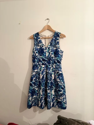 Blåvit blommig klänning från H&M - Superfin blåvit klänning från H&M med blommigt mönster, v-ringning och öppen rygg med snygga banddetaljer. Klänningen är ärmlös och har en utställd kjol som ger en skön och luftig känsla. Perfekt för dig som vill sticka ut med färg och mönster!