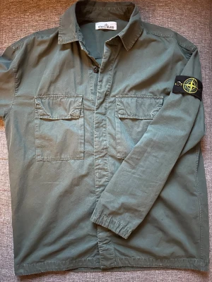 Stone Island overshirt  - Säljer en grön overshirt från Stone Island med klassisk patch på vänster ärm. Jackan har två bröstfickor med lock, skjortkrage och knäppning framtill. Perfekt för vinter och kommande vår.                                                   Nypris: 4000kr 