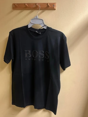 Svart t-shirt från Hugo Boss - Svart t-shirt från Hugo Boss med diskret BOSS-logga framtill i svart ton. Klassisk rund halsringning och korta ärmar. Tillverkad i mjuk bomull för en skön känsla och stilren look.