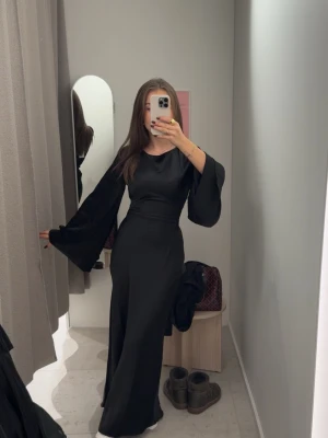 Svart satin maxiklänning med vida ärmar - Supersnygg svart maxiklänning i satin med breda, svepande ärmar och knyt i ryggen. Köpt från Ginatricot & helt slutsåld! Prislappen är kvar, säljer då jag har hittat en annan klänning till julafton!