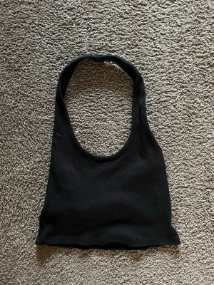 Svart ribbad halterneck linnetopp - Säljer en svart croppad halterneck linnetopp med ribbad struktur. Toppen har en djup rundad halsringning och är ärmlös, perfekt för att styla med jeans eller kjol. Materialet är mjukt och stretchigt, vilket gör den bekväm och snygg för varma dagar.