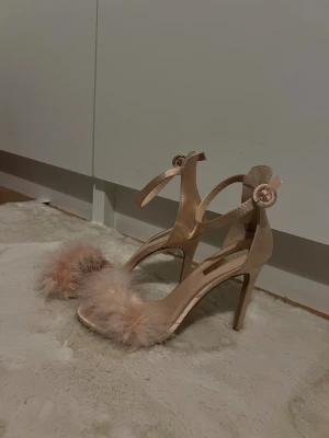 Primark klackar fluffig detalj - Snygga klackar från Primark i ljus beige/rosa hög klack och öppen tå. Remmarna runt ankeln stängs med rund spänne. Perfekta för dig som vill sticka ut med en glam look. Klacken är 11,3 cm hög.