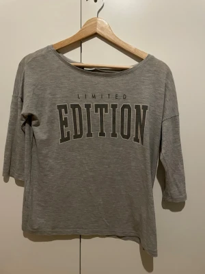 Grå t-shirt med tryck från Gina Tricot - Säljer en grå t-shirt från Gina Tricot i storlek XS med stort tryck 'LIMITED EDITION' på framsidan. T-shirten har trekvartsärm och är gjord i mjuk bomull. Perfekt för dig som gillar en chill och enkel stil.