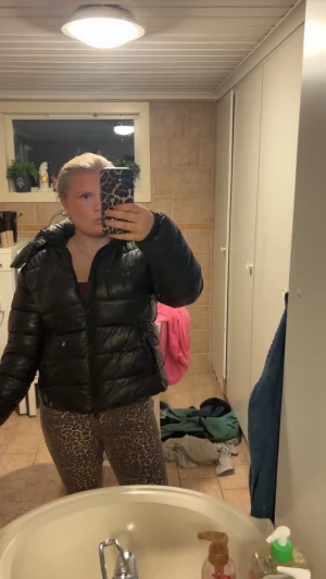 Svart pufferjacka med huva - Säljer en svart pufferjacka med stor, mysig huva och dragkedja framtill. Jackan har quiltad design och är tillverkad i glansig syntet. Perfekt för kalla dagar och har en loose passform som ger en chill vibe. Fickor med dragkedja på sidorna för att hålla dina grejer säkra.