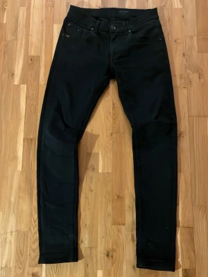 Svarta Slim jeans från Tiger of Sweden - Svarta jeans från Tiger of Sweden med skinny passform och klassisk femficksdesign. Jeansen har svarta bakfickor, silverfärgade nitar och en diskret logotyp vid myntfickan. Materialet är stretchigt jeans och midjan är normal.