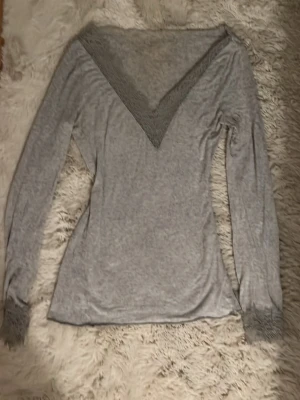 Grå långärmad topp med spets från Intimissimi - Säljer en grå långärmad topp från Intimissimi med snygg v-ringning och spetsdetaljer både vid halsen och ärmsluten. Toppens material är mjukt och stretchigt. 