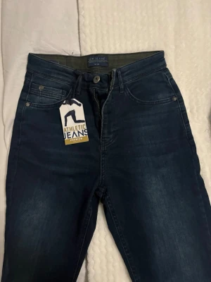 Mörkblå jeans LCW Jeans W28 - Snygga mörkblå jeans från LCW Jeans i storlek W28. Modellen har klassisk femficksdesign, knapp och dragkedja i midjan samt en atletisk passform. Jeansen är tillverkade i stretchigt denim för extra komfort och rörelsefrihet.