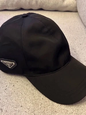 Svart Prada keps - Säljer en helt ny Prada keps, säljer pga att det inte är min stil och inget jag kommer att använda. Nypris: 4000-5500kr Mitt pris: 1899
