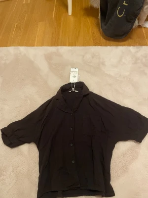 Svart kortärmad skjorta från ONLY XS - Svart skjorta från ONLY i modellen ONLTHYRA med korta ärmar, knappar framtill och en bröstficka. Skjortan är tillverkad i bomull och har en avslappnad passform med klassisk krage. Perfekt för en chill och stilren look.