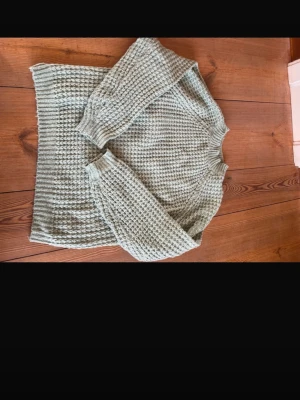 Ljusgrön stickad tröja från 157 - Mysig ljusgrön stickad tröja från 157 i storlek S. Tröjan har ett grovt stickat mönster och ribbad halsringning samt muddar vid ärmslut och nederkant. Perfekt för kyliga dagar och enkel att matcha med jeans eller kjol.