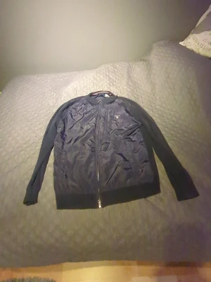 Svart bomberjacka från GANT - Svart bomberjacka från GANT med stilren design. Jackan har glansig framsida i syntetmaterial, ribbade muddar och hel dragkedja. Långärmad och med diskret logga på bröstet. Perfekt för dig som gillar klassisk streetstil.