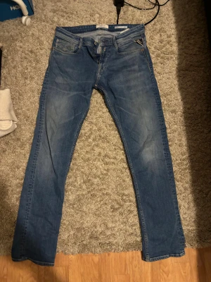 Replay Anbass blå jeans slim fit - Snygga blå Replay Anbass jeans med slim fit och klassisk femficksdesign. Jeansen har en lätt tvättad look, raka ben och normal midja. Materialet är mjukt och stretchigt denim för extra komfort. Perfekt för dig som gillar stilrena och moderna jeans. Storlek W30, L 32.