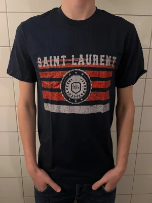 Saint Laurent t shirt  - Riktigt fet och eftertraktad t shirt med saint laurent loggan. Storlek M, skick 10/10!! Modellen på bilden är 183cm. Är lite osäker på äktheten då den saknar tag så därför är priset just nu på 599kr! Nypris runt 4000! Tveka inte med att ställa frågor!