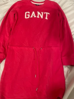 GANT Sweatshirtklänning - Superfin rosa sweatshirtklänning från GANT med broderad logga framtill. Klänningen har långa ärmar, rund halsringning och dragsko i midjan för en snygg passform. Perfekt för en chill och sportig look. PS: Klänningen är i barnstorlek 170 vilket motsvarar S i dam storlek. Priset går självklart att pruta. 