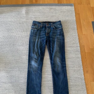 Mörkblå jeans från Nudie Jeans - Snygga mörkblå jeans från Nudie Jeans med klassisk femficksdesign och kontrastsömmar. Jeansen har en rak passform och är tillverkade i slitstarkt denimtyg av bomull. Bakfickorna har Nudie Jeans karakteristiska broderi och läderpatch i midjan.